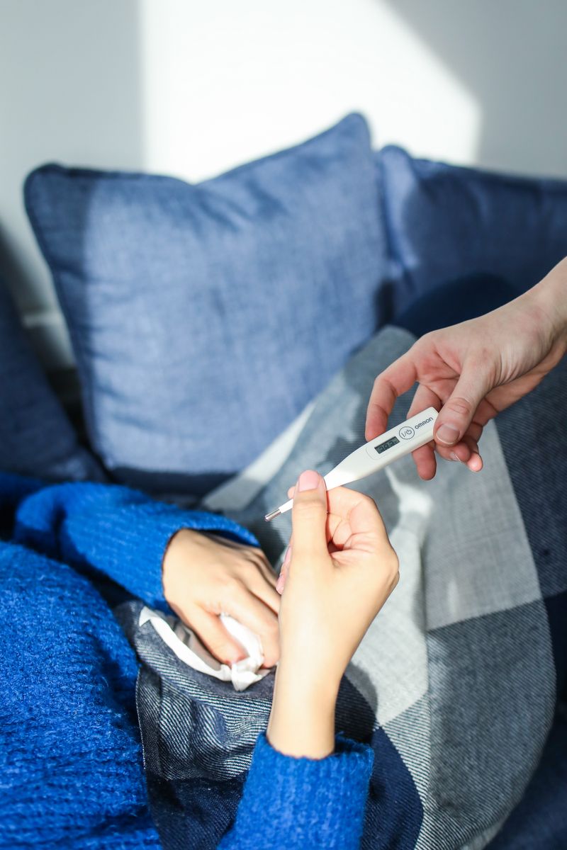 Woman resting on a couch checking her temperature with a digital thermometer