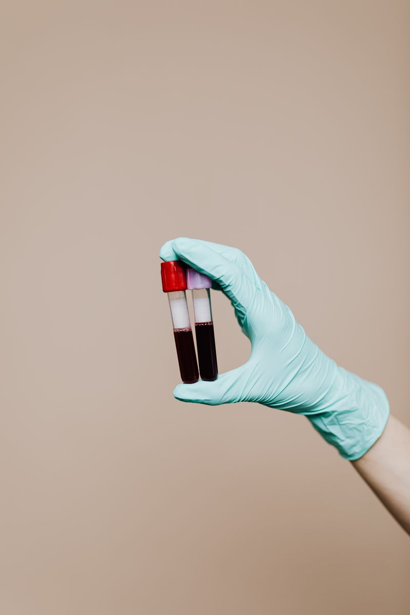 Gloved hand holding blood sample tubes against a neutral background